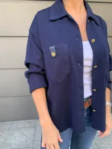 Camisa azul marino de tejido de punto en algodón, con cuello camisero, cierre frontal con botones dorados, bolsillo de parche con solapa de cuero sintético y mangas largas.