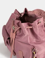 Mochila de tela color lila, con solapa con broche y tira de ajuste, doble bolsillo frontal con broche y pouch con charm lateral en forma de cartera.