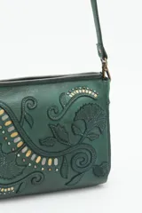 Cartera bandolera verde de cuero vacuno con bordado de flores y tachas doradas y plateadas. Tiene cierre metálico superior, forro de algodón, división interna, bolsillo y tarjetero. La correa es regulable.
