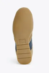 Zapatilla deportiva tipo botín color beige con detalles en azul marino y naranja.