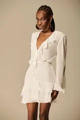 Vestido corto color ivory confeccionado en chiffon, con escote profundo en V enmarcado por volados, mangas largas fluidas y falda con capas de volados.