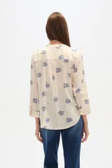 Blusa de manga tres cuartos color crema con estampado floral en azul. Presenta cuello mao con abertura en V y un bolsillo de parche en el pecho.