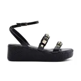 Sandalia de plataforma color negro con tiras finas y apliques de tachas doradas. Cuenta con pulsera al tobillo con hebilla ajustable.