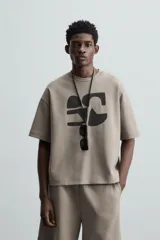 Camiseta color visón de corte relaxed fit, confeccionada en tejido interlock de algodón con elasticidad. Tiene cuello redondo, manga corta y estampado frontal con textura combinada a contraste en color negro.
