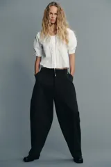 Camisa blanca de cuello bobo con bordados, escote pico con lazada, manga corta abullonada con elástico y cierre frontal con botones.