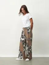 Pantalón de tela color marrón con estampado de flores blancas y negras, de corte palazzo con bolsillos laterales y cintura con cordón.