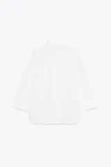 Camisa amarilla de cuello solapa y manga larga acabada en puño. Detalle de bordados perforados a tono. Cierre frontal con botones ocultos por solapa.