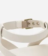 Sandalia plana de cuero sintético color blanco, con tiras superpuestas, detalle de aro metálico y cierre ajustable con hebilla.
