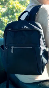 Mochila verde militar de nylon con apertura superior con cierre y tiradores metálicos. Incluye bolsillos internos, bolsillo con cierre metálico al frente, correa corta de mano y correas de galón regulables para colgar en la espalda.