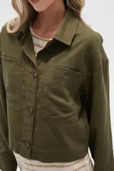 Chaqueta color blanco hueso de lino con cuello camisero, cierre frontal con botones marrones, bolsillos de parche en el pecho y corte holgado.