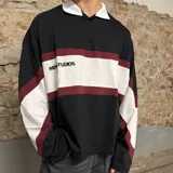 Chomba de manga larga negra con cuello polo blanco, franjas horizontales blancas y bordó, y detalles en blanco en los hombros.