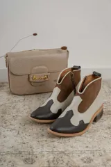 Botines de cuero marrón y blanco con diseño western, puntera redondeada y cierre lateral con cremallera. El talón tiene una tira de cuero para facilitar el calce.
