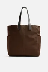 Bolso tipo shopper marrón de tejido de algodón con asas de cuero. Cuenta con dos bolsillos laterales exteriores y un bolsillo interno. Marca Mango.