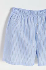 Conjunto de pijama para hombre, compuesto por una remera gris de manga corta con bolsillo en el pecho y un short a rayas verticales celestes y blancas con cintura elástica y botones decorativos.