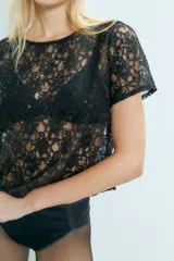 Remera de encaje negro con lentejuelas, cuello bote y mangas cortas.