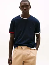 Remera azul marino de algodón con cuello redondo y ribete blanco. Mangas cortas con ribete blanco y rayas rojas y azules. Logo de Tommy Hilfiger bordado en el pecho.