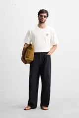 Camiseta blanca de corte holgado, cuello redondo y mangas cortas. Presenta un bordado y estampado combinado en el frente.