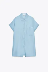 Mono corto de tela celeste, con cuello solapa, mangas cortas con dobladillo y cierre frontal con botones. Tiene un bolsillo de parche en el pecho.