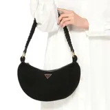 Bolso de hombro tipo media luna, color negro, con acabado de gamuza o material similar. Presenta un cierre superior con cremallera y un logo triangular metálico de Guess en color dorado en el frente. La correa de hombro es negra y trenzada.