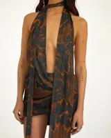 Vestido corto de tela transparente con estampado abstracto en tonos negro, azul oscuro y naranja. Diseño halter con tiras largas que caen al frente y parte inferior fruncida.