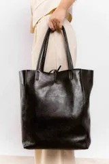 Bolso tote grande de cuero negro con doble asa larga y cierre superior con tira de cuero. Diseño minimalista y atemporal.