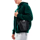 Bandolera negra de poliéster con detalles en cuero sintético. Tiene correa ajustable, cierre superior con cremallera, bolsillos internos y gancho para llaves. El logo de The North Face está estampado en blanco en el frente.