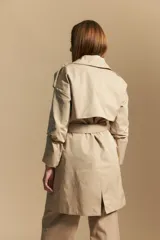 Trench color beige de corte clásico con cuello amplio, botones frontales, detalles en los hombros y mangas largas.