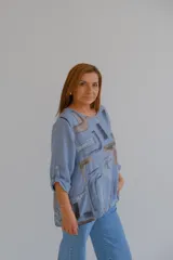 Blusa celeste con estampado abstracto en tonos grises y marrones, de corte holgado, mangas largas con puños abotonados y bolsillos delanteros.