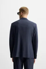 Blazer azul marino con sutil diseño de cuadros, corte regular fit, cuello con solapas de muesca, manga larga con puños abotonados, bolsillo de vivo en el pecho, bolsillos de solapa en la cadera, bolsillo interior, aberturas en la espalda y cierre frontal con dos botones.