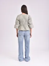 Blusa negra con escote mao y mangas 3/4 con volantes. Presenta detalle de frunces en el frente y lazos para ajustar.