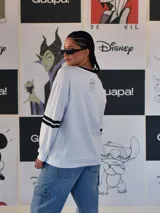 Buzo blanco de manga larga con cuello redondo y puños y ruedo en rib negro. Presenta un gran estampado frontal de la letra 'M' rellena de dibujos de personajes de Disney, incluyendo a Mickey Mouse. Las mangas tienen dos franjas negras a la altura del bíceps.