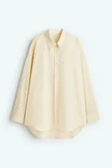 Camisa color crema de tejido fresco de mezcla de algodón, corte amplio, con cuello clásico, cierre frontal con botones, canesú en la espalda, hombros caídos, mangas largas con puños abotonados y bajo redondeado.