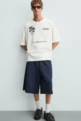 Camiseta blanca de corte holgado, cuello redondo y manga corta. Presenta estampados combinados en negro en la parte delantera y trasera.