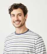 Pijama masculino de dos piezas, compuesto por una remera de manga larga y cuello redondo, y un pantalón largo. La remera es blanca con rayas horizontales en tonos gris, azul marino y verde claro. El pantalón es de color azul jaspeado.