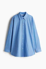 Camisa celeste y blanca a rayas verticales, de corte amplio y mangas largas con puños abotonados. Cuello clásico y cierre frontal con botones.