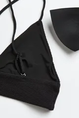 Top de bikini negro con copas de triángulo con relleno extraíble, breteles finos ajustables y tiras cruzadas en la espalda.