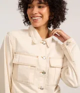 Campera color crudo de manga larga, confeccionada en sarga de algodón, con cuello inglés, abotonada al frente, bolsillos con solapa en el pecho y costuras contrastantes en color marrón.