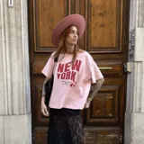 Camiseta rosa de corte amplio con estampado de texto en rojo que dice "New York, Sleepless Nights and City Lights" y dos estrellas.