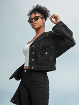 Campera de jean negra con corte cropped, cuello clásico, cierre frontal con botones metálicos y bolsillos con solapa en el pecho.