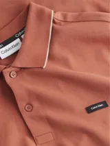 Chomba color ladrillo de piqué de algodón orgánico, corte slim, cuello polo con ribete color crema, tapeta de dos botones, mangas cortas con puños de punto y logo de Calvin Klein en el pecho.