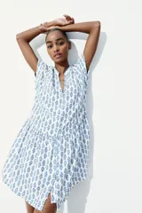 Vestido túnica corto blanco con estampado floral azul, cuello mao y abertura en V. Mangas cortas con doblez, botones forrados y costura fruncida en la cadera. Corte holgado.