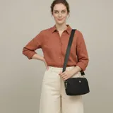 Cartera bandolera negra de lona, con cierre de cremallera, herrajes dorados y correa ajustable.