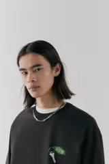 Remera negra de corte holgado y mangas cortas, con cuello redondo y estampado pequeño de llave de hotel en el pecho.