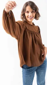 Camisa marrón de poliéster con cuello redondo con volados y mangas largas abullonadas.