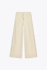 Pantalón de lino color crema, de tiro alto con cintura elástica ajustable con cordón, pinzas delanteras, bolsillos laterales y traseros. Piernas anchas.