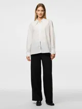 Camisa blanca de corte holgado, con cuello clásico, mangas largas con puños abotonados y cierre frontal con cremallera.