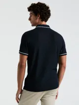 Polo de piqué azul marino con vivos blancos en cuello y mangas, calce slim fit y logo bordado en el pecho.