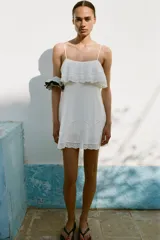 Vestido corto blanco con tirantes finos ajustables, escote recto, detalle de bordados y volantes, tejido elástico tipo nido de abeja y forro interior combinado a tono.