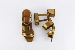 Sandalias negras de cuero con dos tiras sobre el empeine y pulsera al tobillo con ojalillos y tachas. Taco cuadrado de 5 cm.