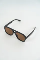 Lentes de sol estilo aviador con montura gruesa de acetato color negro y lentes marrones.